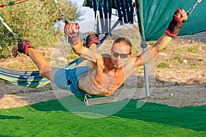 Yoga treatment for core, yoga swing, slim young man strapped to four planks above the ground, man developing endurance