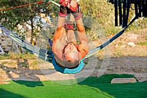Yoga treatment for core, yoga swing, slim young man strapped to four planks above the ground, man developing endurance