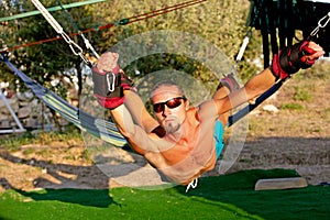 Yoga treatment for core, yoga swing, slim young man strapped to four planks above the ground, man developing endurance