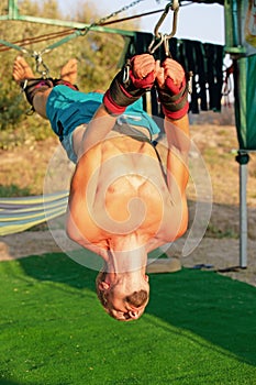 Yoga treatment for core, yoga swing, slim young man strapped to four planks above the ground, man developing endurance