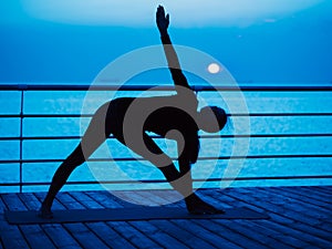 Yoga under full moon over night ocean or sea beach. Young woman`s meditation during practice.