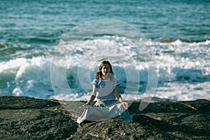Yoga woman meditates sitting on rocks on the Alantic ocean coast.