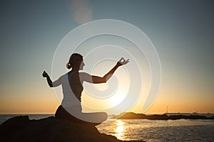 Yoga woman meditating in the lotus position during sunset on the oceanfront.