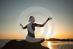 Yoga woman meditating by the sea during sunset.