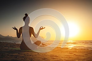 Yoga woman meditating at serene sunset or sunrise on the beach. The girl relaxes in the lotus position. Fingers folded