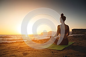 Yoga woman meditating at serene sunset or sunrise on the beach. The girl relaxes in the lotus position. Fingers folded