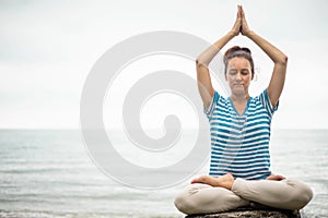 Yoga woman meditation in lotus position at pebble sea beach sunset sky horizon healthy lifestyle