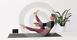 Yoga woman performs Paripurna Navasana exercise, boat pose with alternating leg lifts and foot warm-up