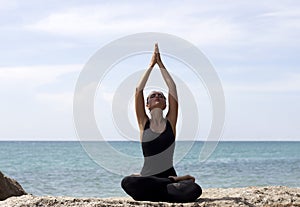 Yoga woman poses on beach near sea and rocks