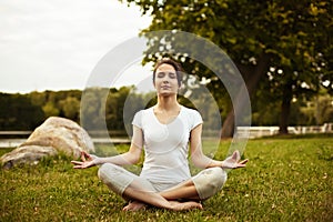 Yoga woman sitting on the grass in lotus pose in park.