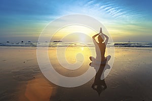 Yoga woman sitting in lotus pose on the beach with reflection during sunset.