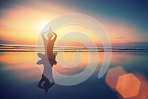 Yoga woman sitting in lotus pose on the beach with reflection in water.