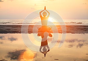 Yoga woman sitting in lotus pose on the beach during sunset, with reflection in water.