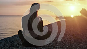 Yoga woman sitting in lotus position turning head at sunrise beach. 4k Dragon RED camera