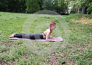 Yoga woman with tattos and mask doing Sphinx exercise in park nature.