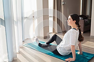 Yoga. A young woman sitting resting on a mat, and looks out the window. The concept of home workouts