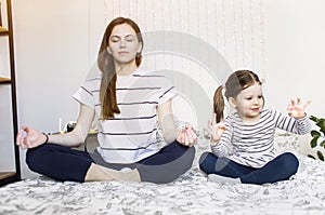 Yoga. Young woman and small daughter doing yoga lotus position in bed. relaxation and meditation at home in isolation