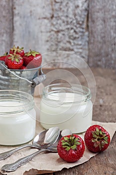 yoghurt in a glass and a bucket with fresh strawberries on a woo