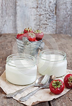 yoghurt in a glass and a bucket with fresh strawberries on a woo