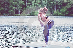 Yogi  girl  practicing yoga, standing in Eagle pose, Garudasana exercise on the lake. Concept of healthy life and natural
