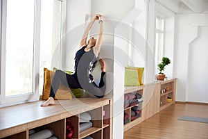 Yogi woman in dark tracksuit preparing to yoga practicing, warm up her body stretching backwards in white studio space