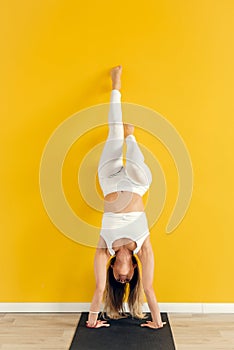 Yogini practicing yoga pose in the gym. The woman stands upside down