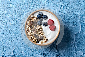 Yogurt with berries and muesli for breakfast in bowl on lbue background