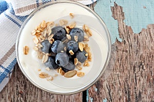 Yogurt with blueberries, granola, close up over a wooden background