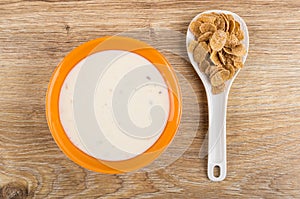 Yogurt in bowl, multicereal flakes in plastic spoon on table