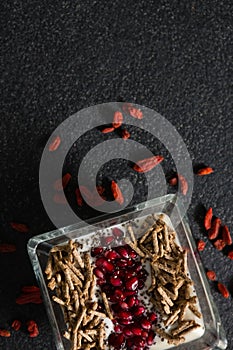 Yogurt, cereal bran sticks and pomegranate seeds in tray with dried fruits