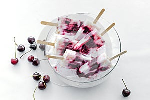 Yogurt and cherries popsicles in a bowl on white background.