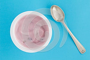 Yogurt cup with strawberry yoghurt in small plastic cup and vintage silver spoon on bright blue background - top view photo