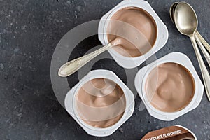 Yogurt cups with chocolate flavoured yoghurt on dark grey background with spoons - top view photo