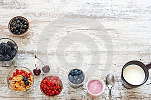 Yogurt, fresh berries, cornflakes and cup of milk on a wooden table.