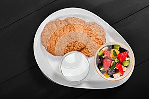 Yogurt with fruit salad and oat cookies on plate on dark wooden background. Fresh healthy breakfast