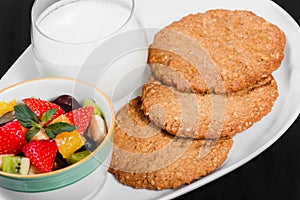 Yogurt with fruit salad and oat cookies on plate on dark wooden background. Fresh healthy breakfast