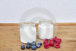 Yogurt in glass jar, raspberries and blueberries on a wooden background - horizontal