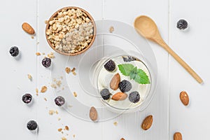 Yogurt with granola, blackberries and almonds on a white wooden table.