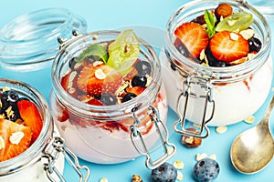 Yogurt with granola, fresh berries and nuts in a jar on a blue background. Healthy breakfast and milk dessert concept