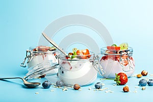Yogurt with granola, fresh berries and nuts in a jar on a blue background. Healthy breakfast and milk dessert concept