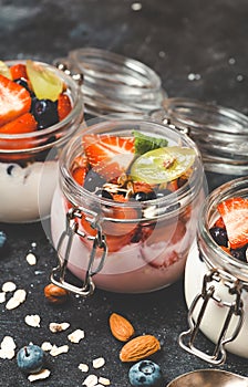 Yogurt with granola, fresh berries and nuts in a jar on a dark background. Healthy breakfast and dessert concept
