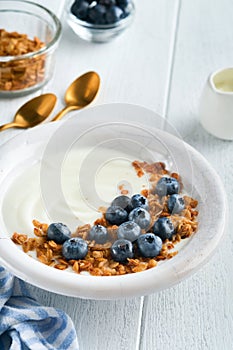 Yogurt. Greek Yogurt with granola and fresh blueberries in white bowl over old white wood background. Morning breakfast concept. H