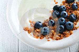 Yogurt. Greek Yogurt with granola and fresh blueberries in white bowl over old white wood background. Morning breakfast concept. H