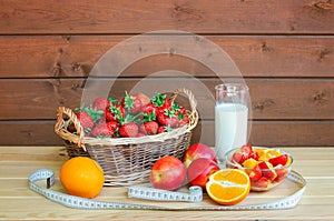 Yogurt, healthy fruit salad, fresh fruits, wicker basket of fresh strawberry, and measuring tape on wooden table. Healthy eating