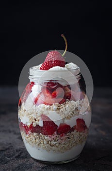 Yogurt oat granola with strawberries, in a glass jar on black backdrop,