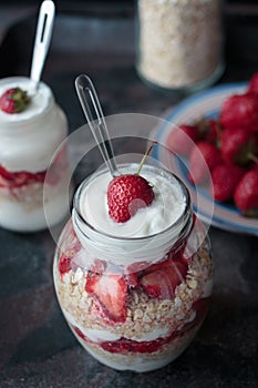 Yogurt oat granola with strawberries, in a glass jar on black backdrop,