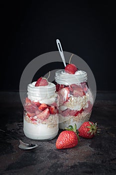Yogurt oat granola with strawberries, in a glass jar on black backdrop,