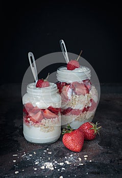 Yogurt oat granola with strawberries, in a glass jar on black backdrop,