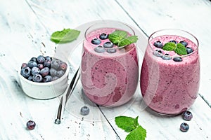 Yogurt smoothies fresh blueberries in glass with mint leaf and raw beeries on light background. Restaurant menu, dieting, cookbook photo