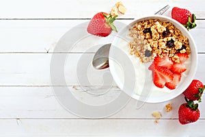 Yogurt with strawberries & granola, flat lay, side orientation over white wood.